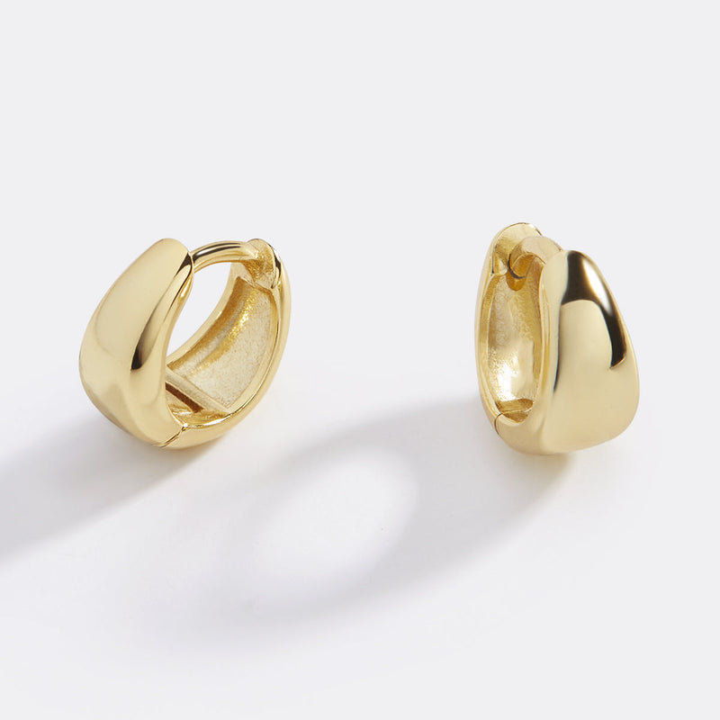 Astra Teardrop Huggies — A pair of gold huggie hoop earrings with a teardrop design on a black background.