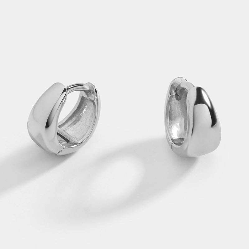 Astra Teardrop Huggies — A pair of gold huggie hoop earrings with a teardrop design on a black background.