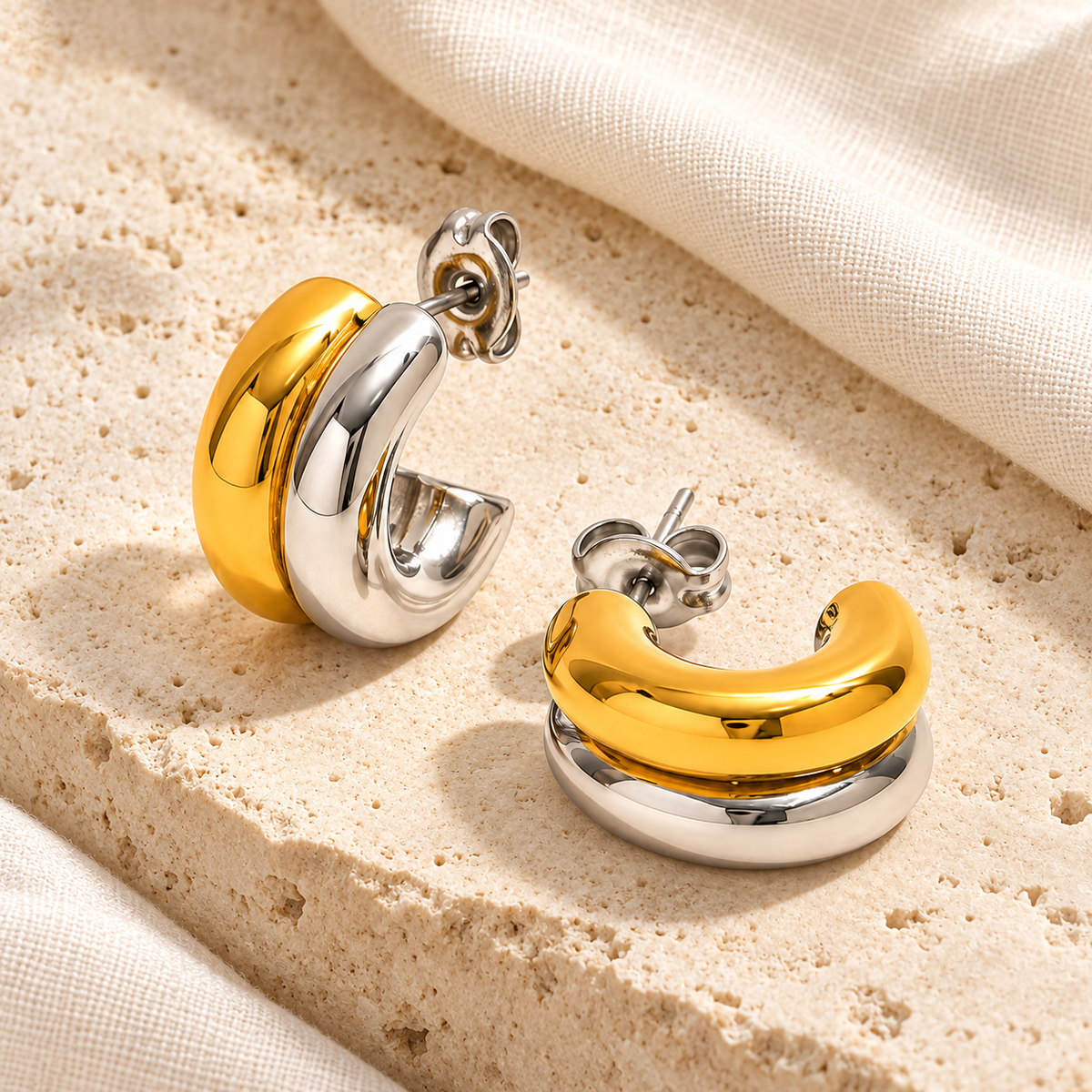Duet two-tone earring pair on pale limestone beside ivory linen