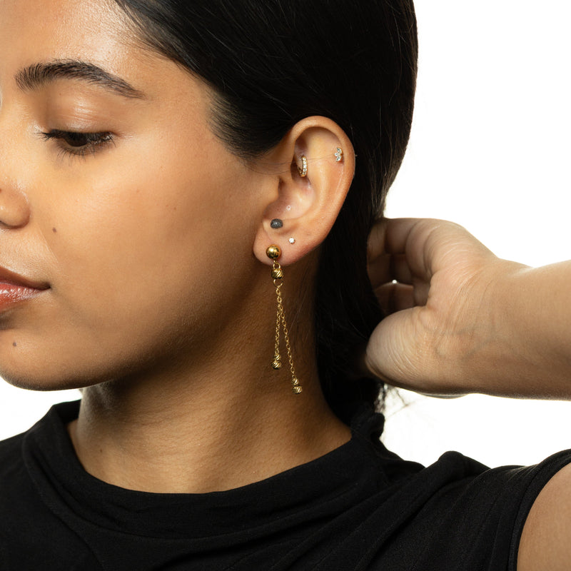 Noor Chain Drop Earrings — Woman in side profile wearing gold drop earrings with dual chains and ribbed beads, hand resting near the back of her head.