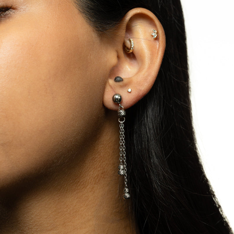 Noor Chain Drop Earrings — Woman wearing a single silver earring with double chain dangles ending in ribbed bead charms.