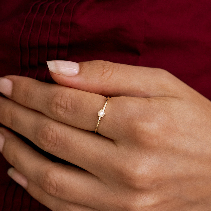 Seren Pearl Stacking Ring — Gold ring with a pearl on a person's finger against a red fabric background