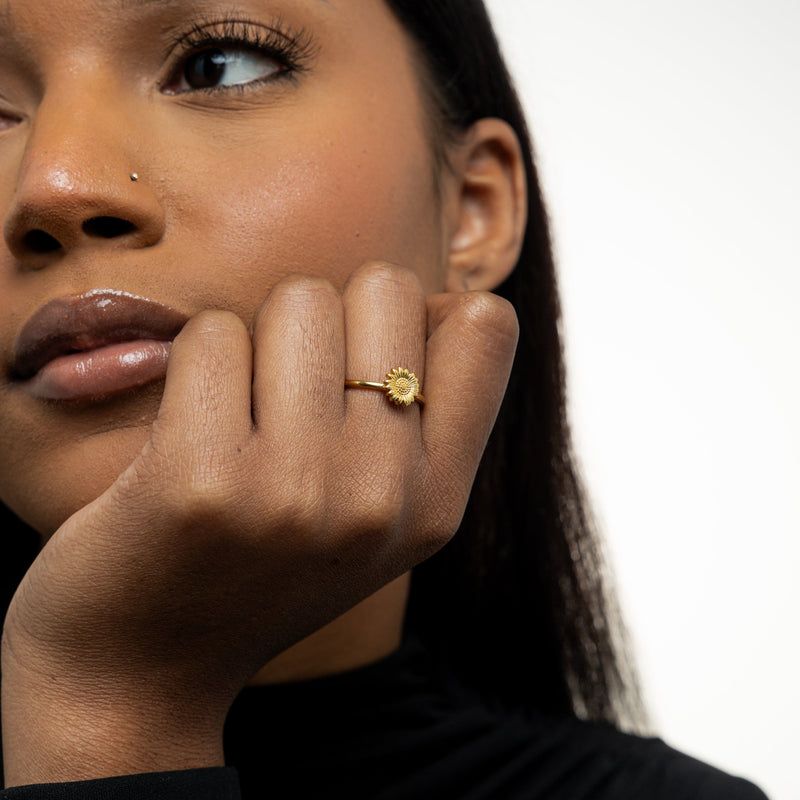 Woman wearing a gold Solara Bloom Ring on her finger, hand resting near her face.