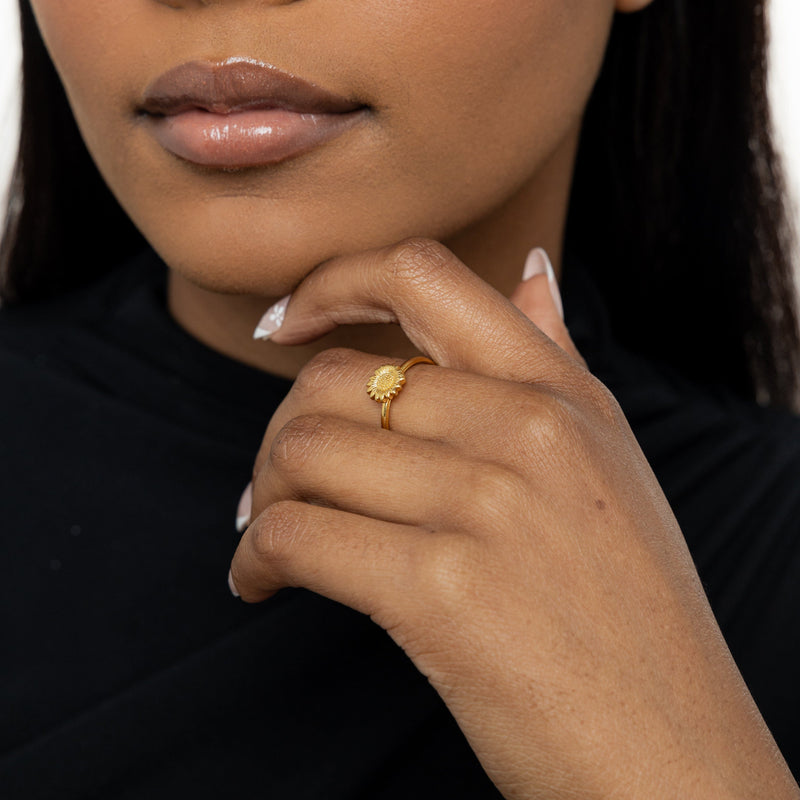 Woman wearing a gold Solara Bloom Ring, hand gently resting against her chin